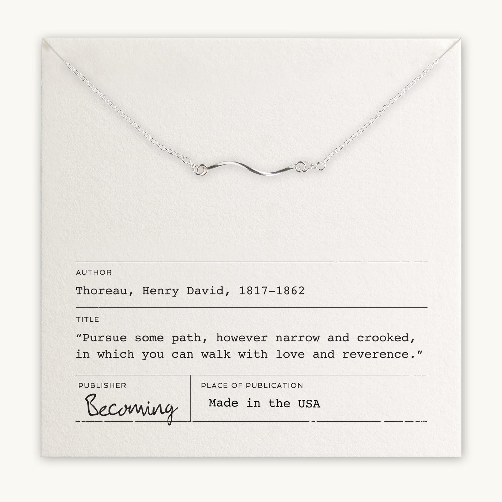 A Path Necklace with a curved path charm in gold filled displayed on a card featuring a quote by Henry David Thoreau, with the mention 