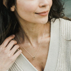 Woman wearing a delicate Becoming Jewelry Together Forever Necklace and a beige cardigan, smiling slightly off-camera.