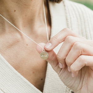 A person holding a Loved Necklace pendant necklace with a mountain landscape design by Becoming Jewelry.