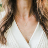 Woman wearing a Becoming Jewelry Pillar of Strength Necklace with a hammered bar drop charm paired with a white knitted top.