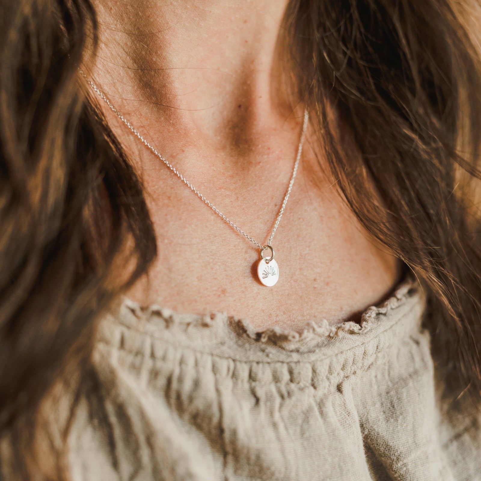 A close-up of a woman wearing a delicate You Are My Sunshine Necklace by Becoming Jewelry with a small, round sunshine charm pendant.