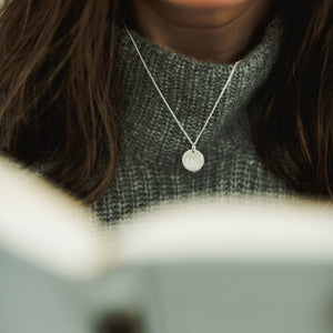 A person wearing a gray sweater and a Trees Necklace with a trees charm pendant from Becoming Jewelry.
