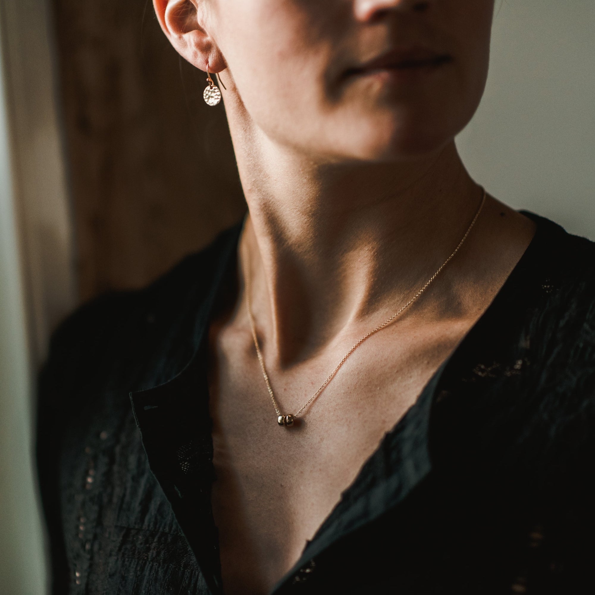 A person wearing a black textured top, a Friends Beads Necklace from Becoming Jewelry, and a pair of earrings. Their face is partially visible, with neutral lighting in the background—a perfect snapshot of friendship and the meaningful gift of togetherness.