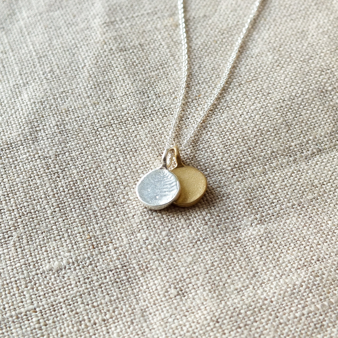 A Count My Blessings Necklace by Becoming Jewelry with two round silver &amp; gold vermeil charms on a linen background.