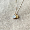 A Count My Blessings Necklace by Becoming Jewelry with two round silver & gold vermeil charms on a linen background.