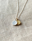 A Count My Blessings Necklace by Becoming Jewelry with two round silver & gold vermeil charms on a linen background.