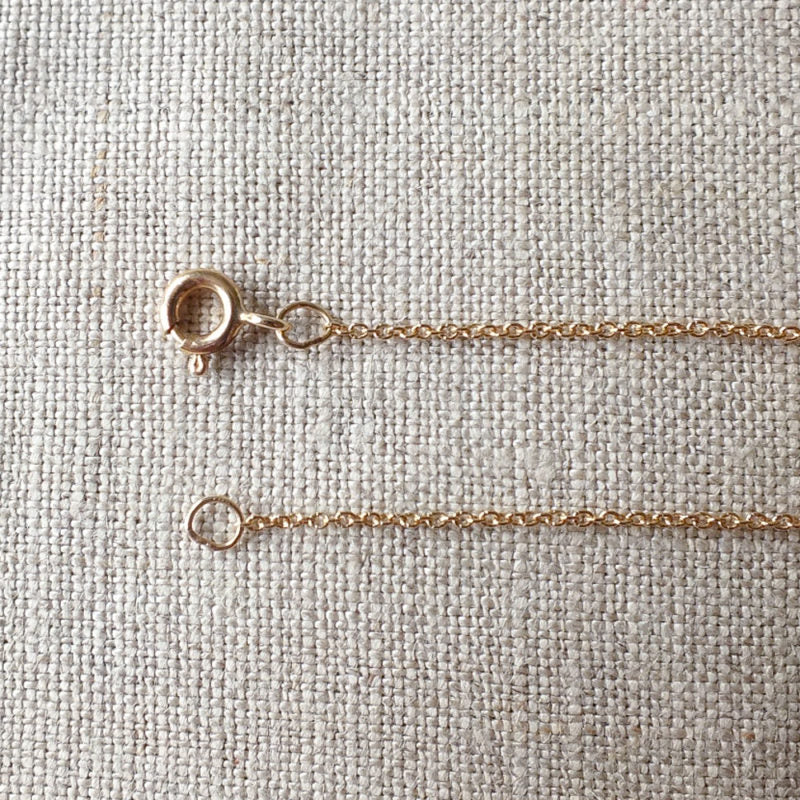 Close-up of a Becoming Jewelry Replacement Chain, Gold clasp and chain laid on a textured beige fabric surface.