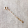 A short gold Chain Extender by Becoming Jewelry, featuring a round clasp and a subtle chain extender, resting on a textured beige fabric surface.