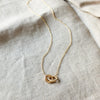 A Linked By Blood Necklace by Becoming Jewelry with a knot pendant lying on a fabric surface.