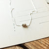 A delicate Three Things Necklace by Becoming Jewelry with three small beads displayed on a piece of paper with lines.