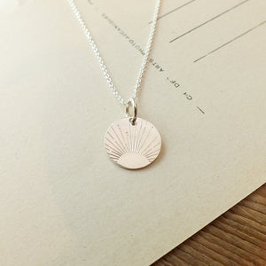 Becoming Jewelry's Irish Blessing Necklace with a sun charm design on a piece of paper.