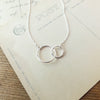 Silver interlocked circles pendant necklace, a perfect Becoming Jewelry mother's necklace, displayed on a vintage postcard.