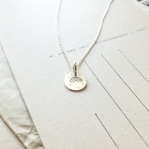 Over the Rainbow Necklace by Becoming Jewelry, featuring a stamped design, resting on a sheet of paper with printed text.
