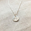 Becoming Jewelry's You Are My Sunshine Necklace features a sterling silver pendant with a Sunshine Charm design on a textured fabric surface.