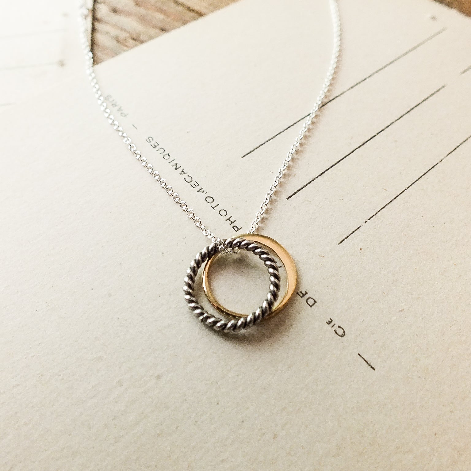 Becoming Jewelry True Friends Necklace with a twisted ring pendant on a piece of paper.