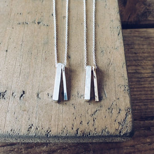 Two Through Thick & Thin Necklaces by Becoming Jewelry, featuring mixed metal charms, on a wooden surface.
