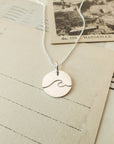 Ocean Wave Round Charm Necklace pendant on a chain, displayed on vintage postcards by Becoming Jewelry.