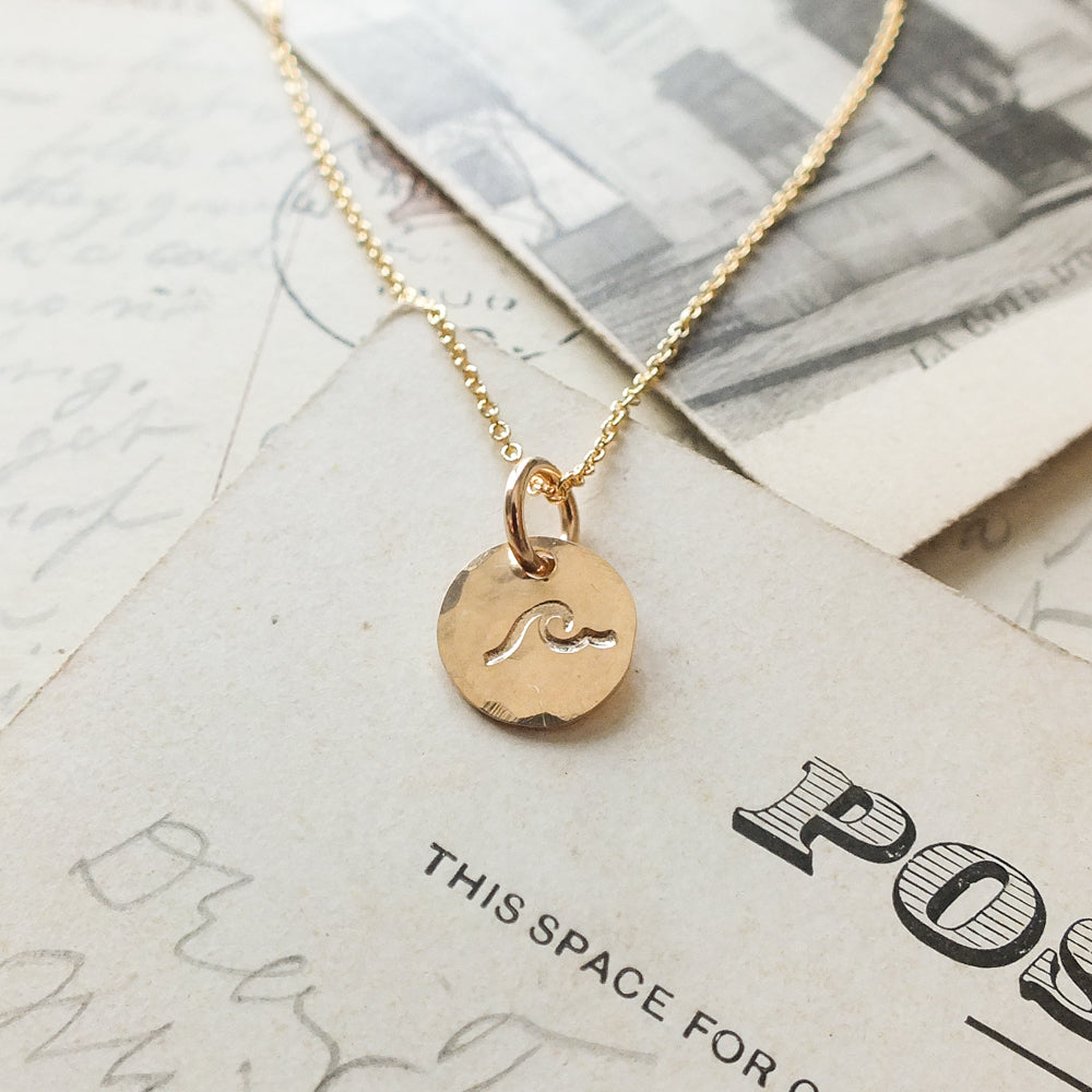 Becoming Jewelry&#39;s Swim the Sea Necklace with a wave charm design displayed on a piece of paper.