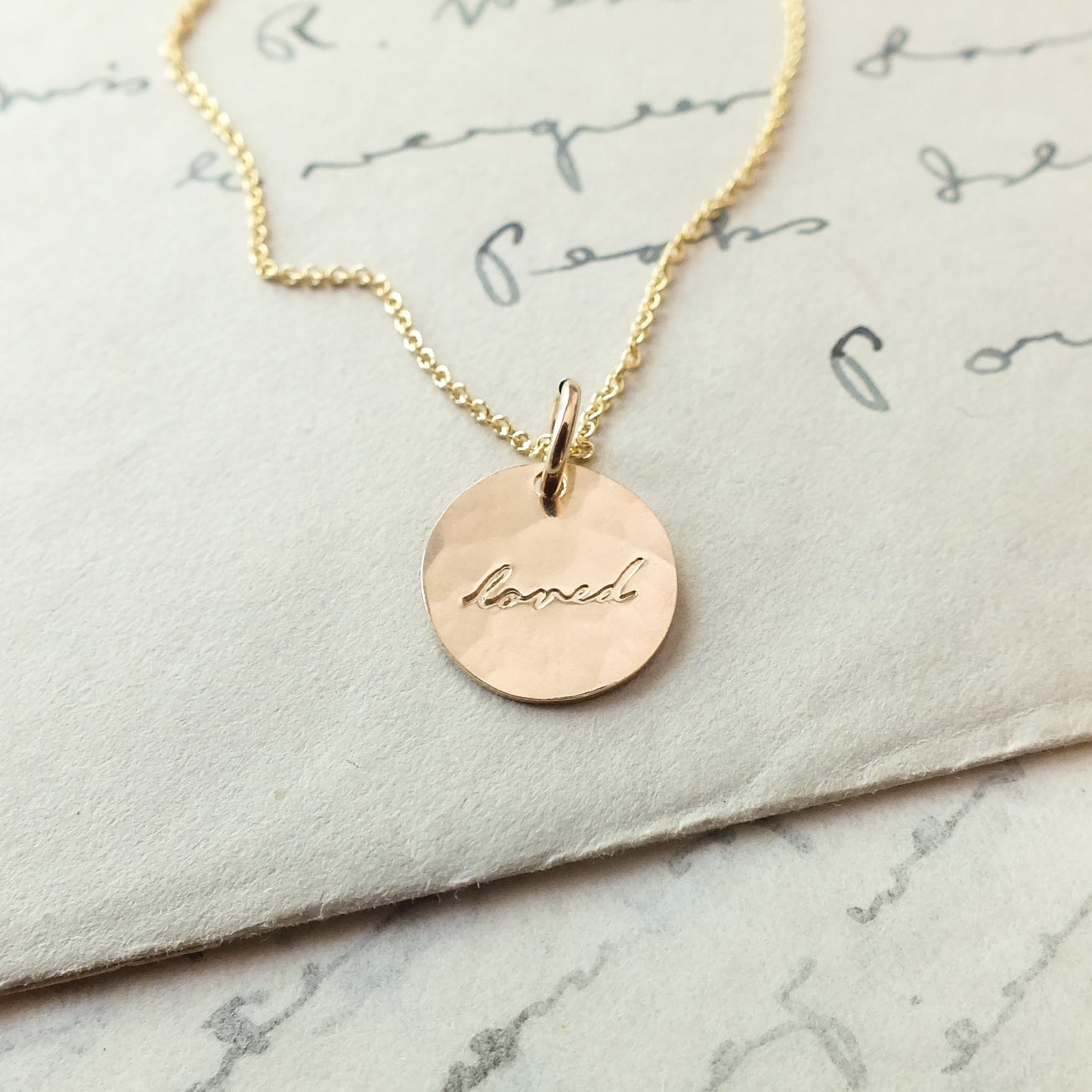 Becoming Jewelry&#39;s Loved Necklace, a sterling silver pendant necklace with the word &#39;laugh&#39; engraved, lying on a handwritten letter.