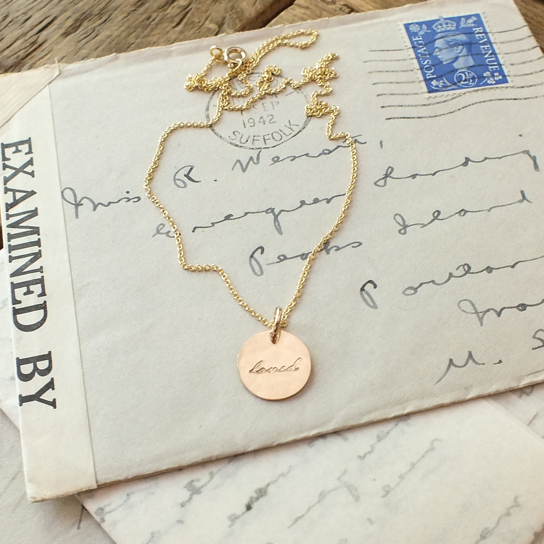 A Loved Necklace by Becoming Jewelry with a circular pendant inscribed with the name &quot;linda&quot; resting on top of an old, handwritten letter.