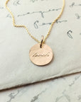 Becoming Jewelry's Loved Necklace, a sterling silver pendant necklace with the word 'laugh' engraved, lying on a handwritten letter.