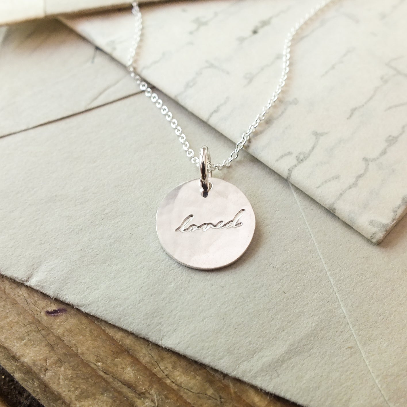 Becoming Jewelry&#39;s Loved Necklace with the word &quot;love&quot; inscribed, resting on an envelope.