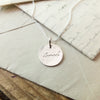 Becoming Jewelry's Loved Necklace with the word "love" inscribed, resting on an envelope.