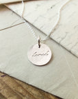 Becoming Jewelry's Loved Necklace with the word "love" inscribed, resting on an envelope.