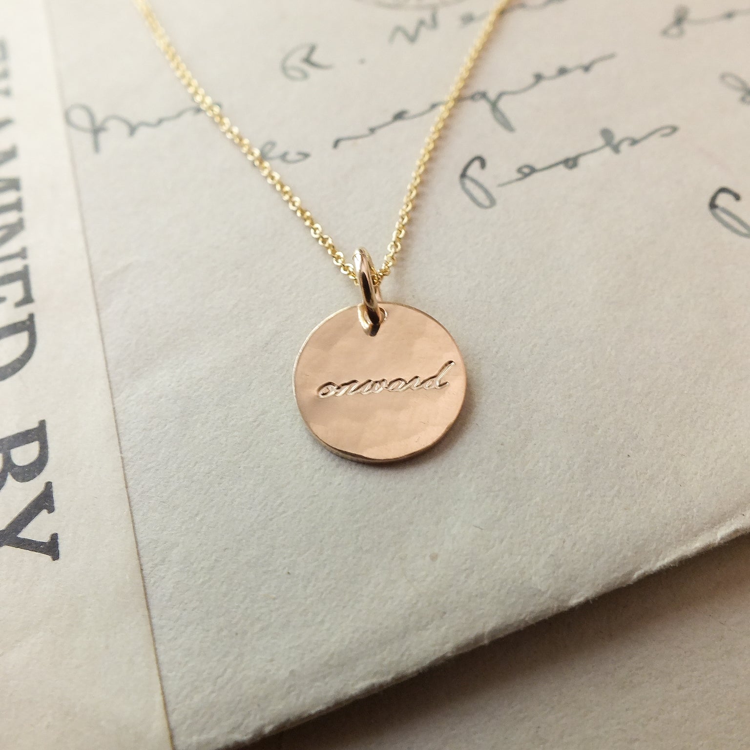 A Becoming Jewelry Onward Necklace with the word "onward" engraved on it, displayed on a piece of paper with cursive handwriting.