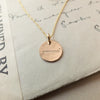 A Becoming Jewelry Onward Necklace with the word "attitude" engraved on it, displayed on a piece of paper with cursive handwriting.