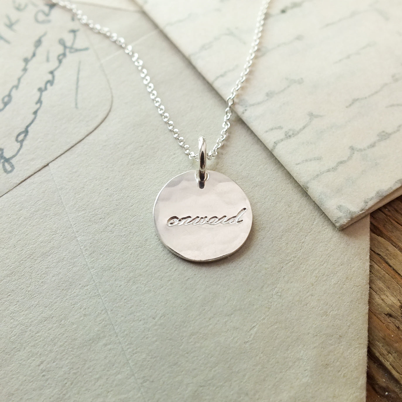 Circular Onward Necklace by Becoming Jewelry on a wooden surface with handwritten letters in the background.